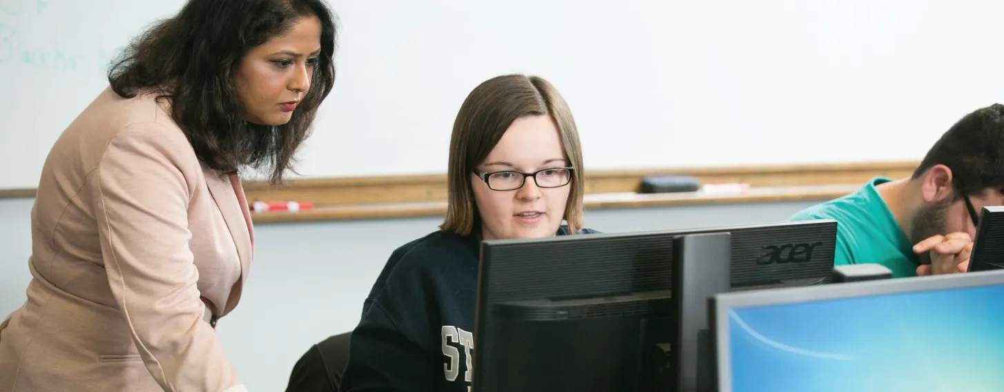 A woman helping a student on a computer in a classroom.